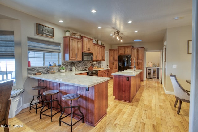 kitchen featuring a peninsula, black appliances, light wood-style floors, brown cabinets, and backsplash