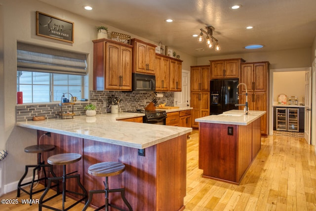 kitchen with light wood finished floors, beverage cooler, light countertops, a peninsula, and black appliances