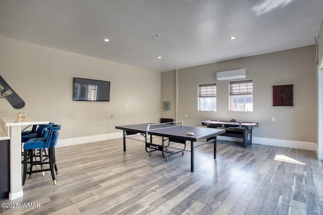 recreation room featuring light wood-type flooring, a textured ceiling, a wall unit AC, recessed lighting, and baseboards