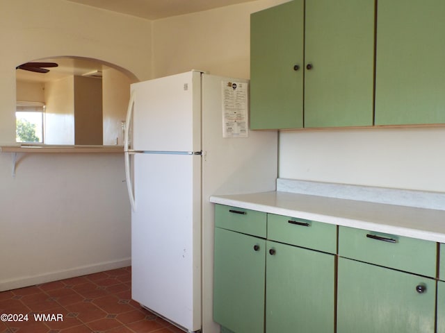 kitchen with arched walkways, light countertops, freestanding refrigerator, green cabinetry, and baseboards