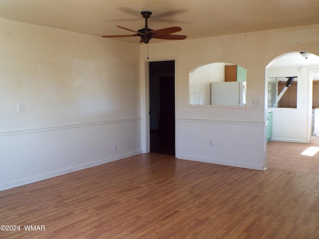 spare room with wood finished floors, a ceiling fan, and baseboards