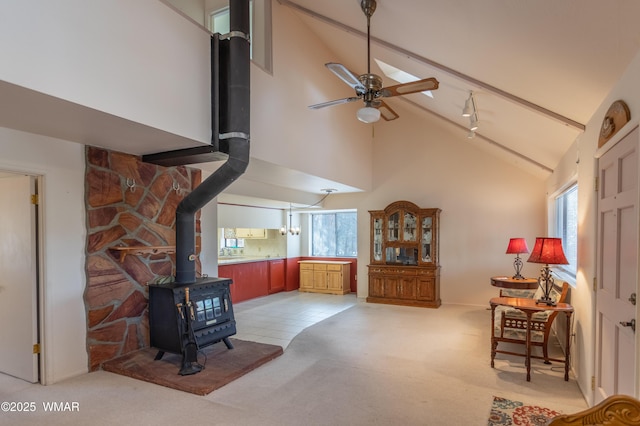 living area featuring light colored carpet, ceiling fan, beamed ceiling, a wood stove, and high vaulted ceiling