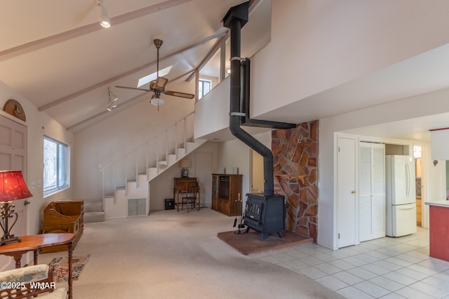 living room with ceiling fan, a wood stove, stairs, high vaulted ceiling, and beam ceiling