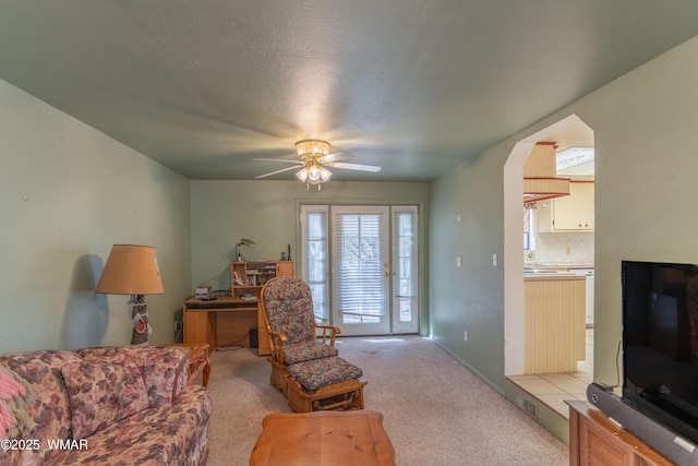 living room featuring light carpet, ceiling fan, and arched walkways