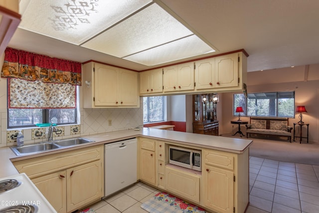 kitchen featuring dishwasher, stainless steel microwave, a peninsula, light countertops, and a sink