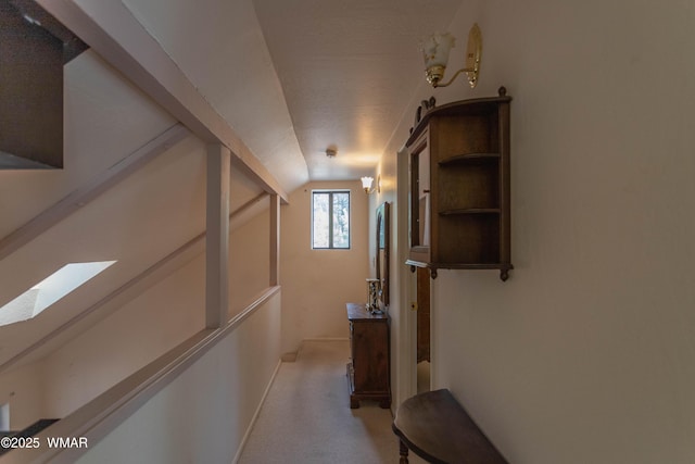 hallway featuring vaulted ceiling and light colored carpet