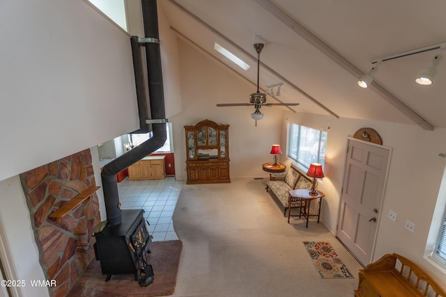 living area with light tile patterned floors, vaulted ceiling with skylight, light carpet, a ceiling fan, and a wood stove