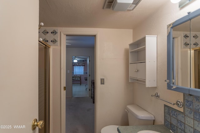 bathroom with a textured ceiling, toilet, visible vents, vanity, and an enclosed shower