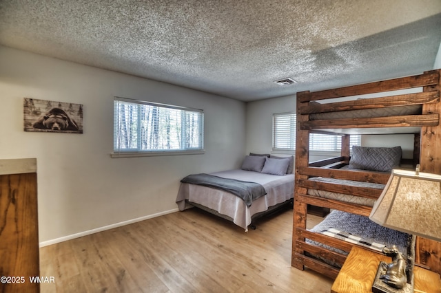 bedroom featuring light wood-style floors, baseboards, visible vents, and a textured ceiling