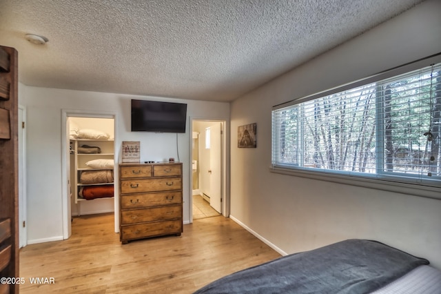 bedroom featuring a textured ceiling, a closet, a walk in closet, and light wood-style floors