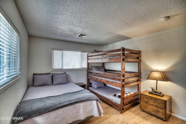 bedroom with a textured ceiling, light wood finished floors, and visible vents