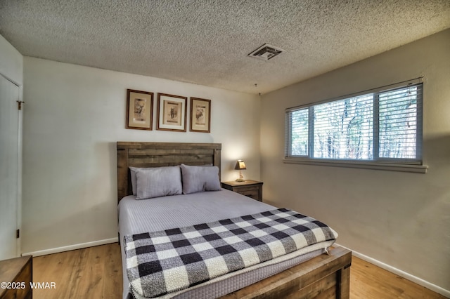 bedroom featuring light wood-type flooring, visible vents, a textured ceiling, and baseboards