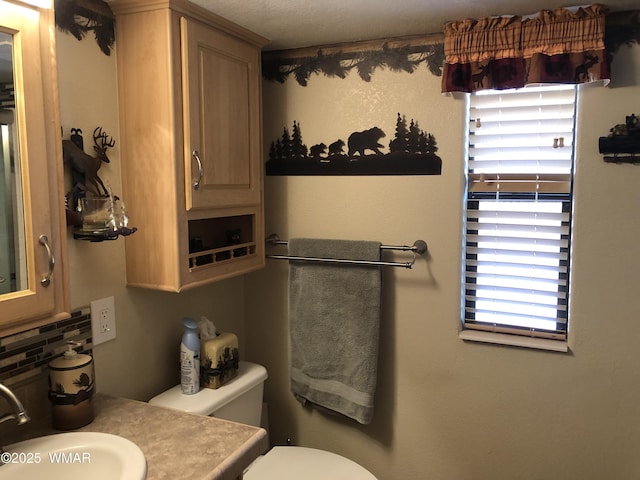 half bathroom featuring toilet, decorative backsplash, and vanity