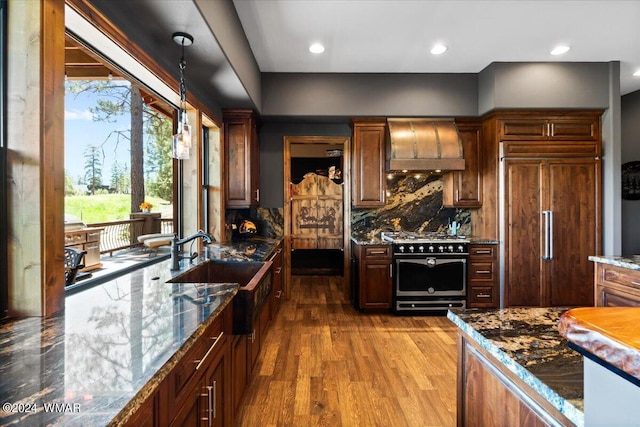 kitchen featuring high end appliances, hanging light fixtures, a sink, wood finished floors, and wall chimney exhaust hood