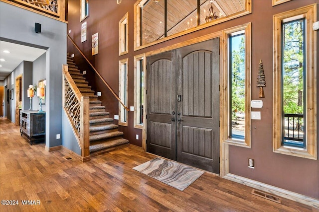 foyer featuring stairs, a towering ceiling, wood finished floors, and visible vents