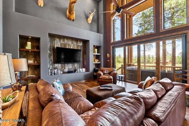 living room featuring built in shelves, a ceiling fan, a high ceiling, and wood finished floors