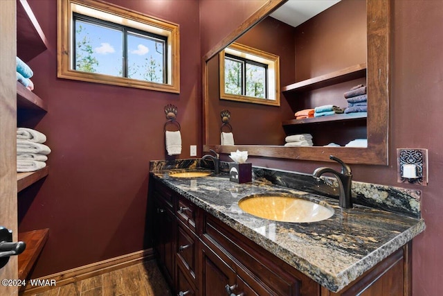 bathroom with wood finished floors, a sink, baseboards, and double vanity