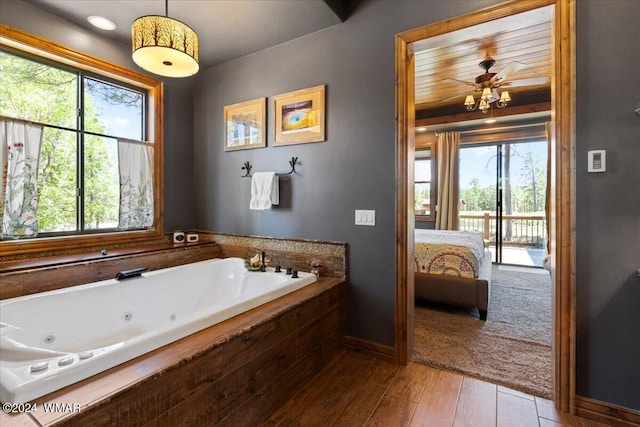 bathroom with ensuite bathroom, wood finished floors, a ceiling fan, baseboards, and a whirlpool tub