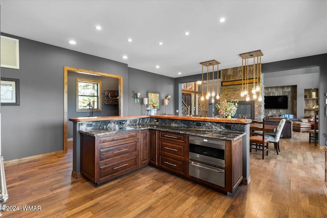 kitchen featuring hanging light fixtures, a warming drawer, dark stone countertops, and wood finished floors