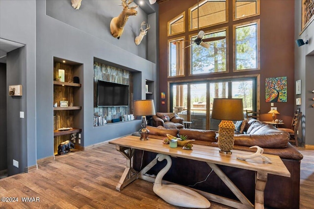 living room with a towering ceiling, a ceiling fan, wood finished floors, and built in features