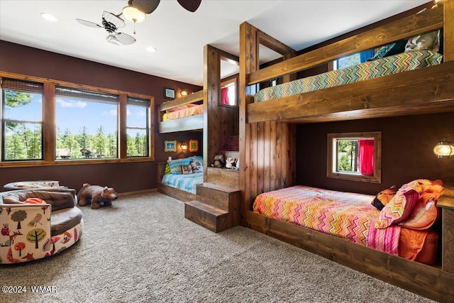 carpeted bedroom featuring wood walls, multiple windows, and a ceiling fan