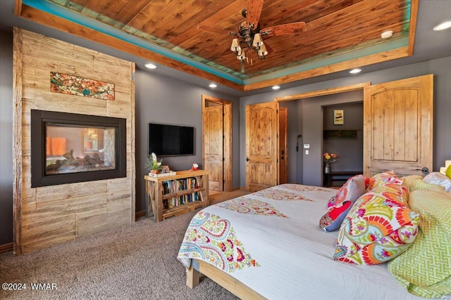 bedroom with wood ceiling, carpet, a tray ceiling, a multi sided fireplace, and recessed lighting