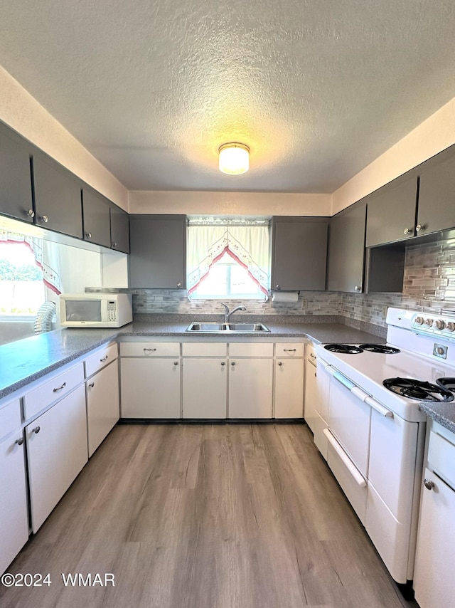 kitchen featuring white appliances, backsplash, light wood-style floors, and a sink