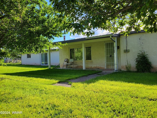 rear view of property with metal roof, a lawn, and stucco siding