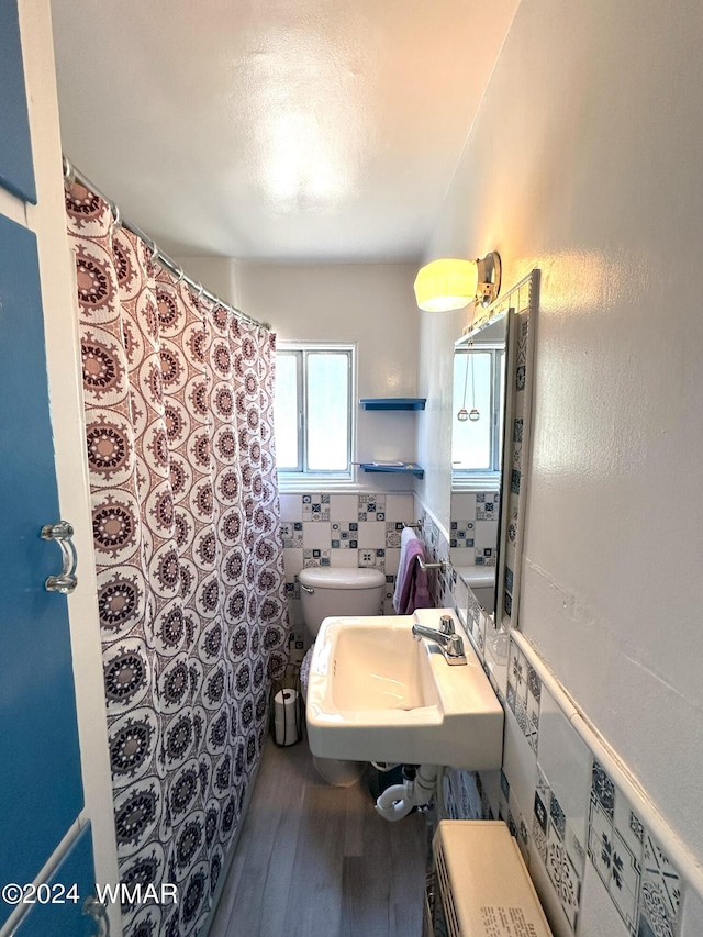 bathroom with toilet, tile walls, a sink, and wood finished floors