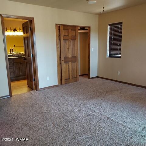 unfurnished bedroom featuring light carpet, a closet, ensuite bath, and baseboards