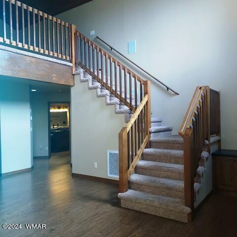 stairs featuring visible vents, wood finished floors, a towering ceiling, and baseboards