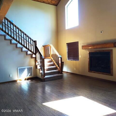 unfurnished living room featuring visible vents, dark wood finished floors, baseboards, stairway, and a high ceiling