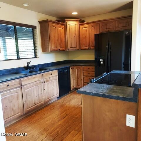 kitchen featuring dark countertops, brown cabinets, a sink, and black appliances