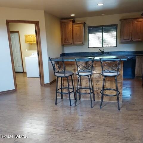 kitchen featuring dark countertops, washer / clothes dryer, dishwasher, and a kitchen breakfast bar