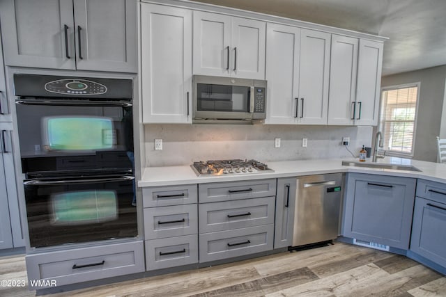 kitchen with appliances with stainless steel finishes, a sink, light wood-style floors, light countertops, and white cabinets