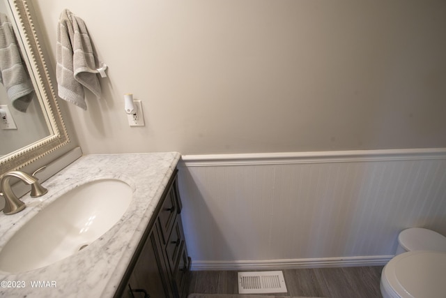 bathroom featuring wainscoting, vanity, wood finished floors, and toilet
