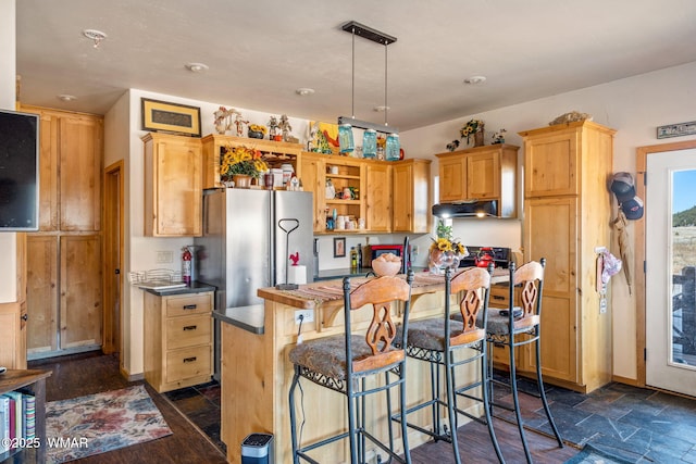 kitchen with a breakfast bar, dark countertops, hanging light fixtures, a kitchen island, and under cabinet range hood