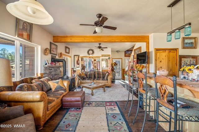 living area featuring ceiling fan, a wood stove, dark wood-style flooring, and beam ceiling