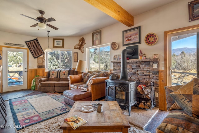 living area featuring a ceiling fan, wainscoting, beamed ceiling, a wood stove, and wood walls