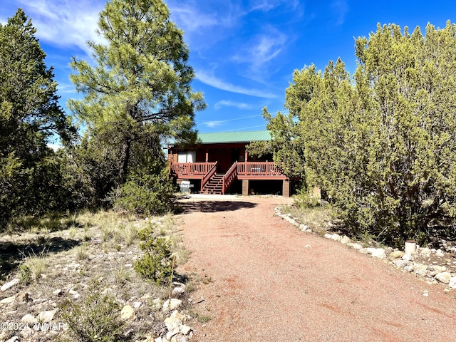 view of front of home featuring metal roof, stairs, dirt driveway, and a deck