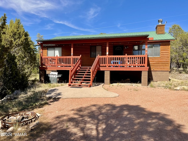 view of front of property featuring log veneer siding, a chimney, metal roof, stairs, and a wooden deck