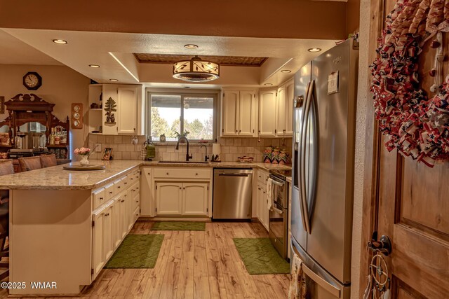 1092 Cedar Dr, Show Low, AZ 85901 - kitchen with stainless steel appliances, a sink, a peninsula, light wood-style flooring, and tasteful backsplash
