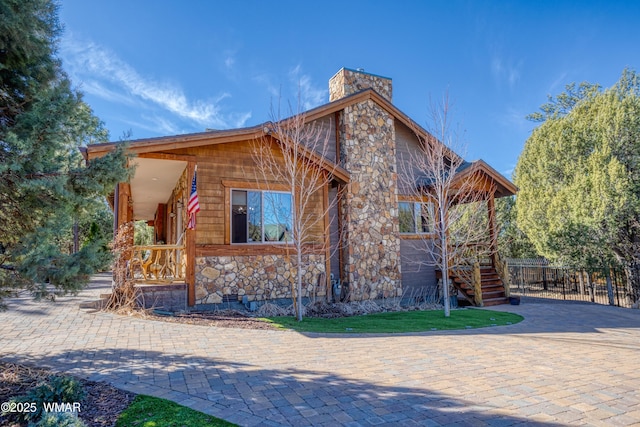 view of front of home with stone siding, a chimney, crawl space, stairs, and fence