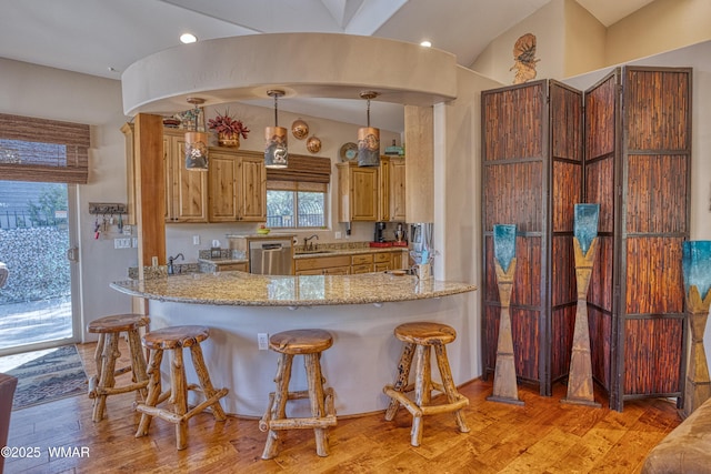 kitchen featuring decorative light fixtures, light stone countertops, light wood-type flooring, stainless steel dishwasher, and a sink