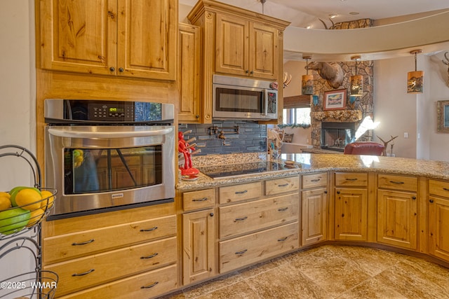 kitchen with decorative backsplash, light stone counters, vaulted ceiling, stainless steel appliances, and a stone fireplace