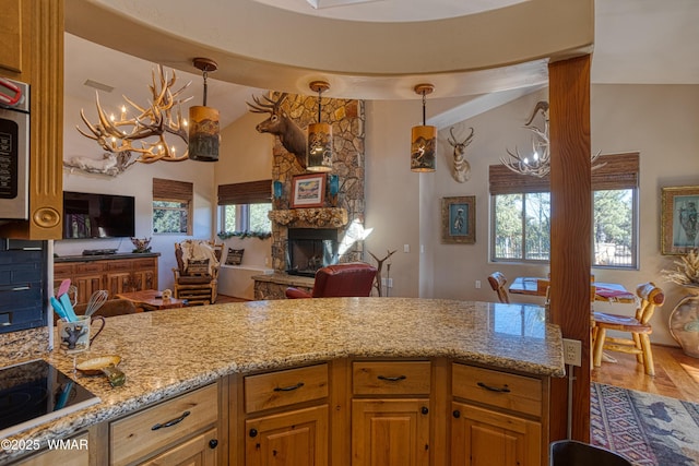 kitchen with lofted ceiling, open floor plan, a stone fireplace, light stone countertops, and black electric cooktop