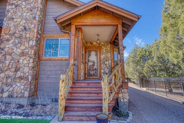 entrance to property featuring stone siding and fence