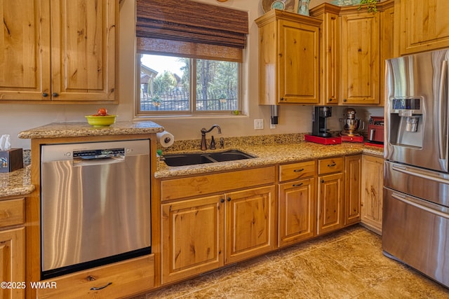 kitchen featuring brown cabinetry, appliances with stainless steel finishes, light stone counters, and a sink