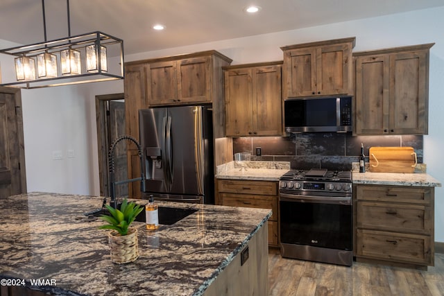 kitchen with dark stone counters, decorative backsplash, appliances with stainless steel finishes, hanging light fixtures, and light wood-style floors