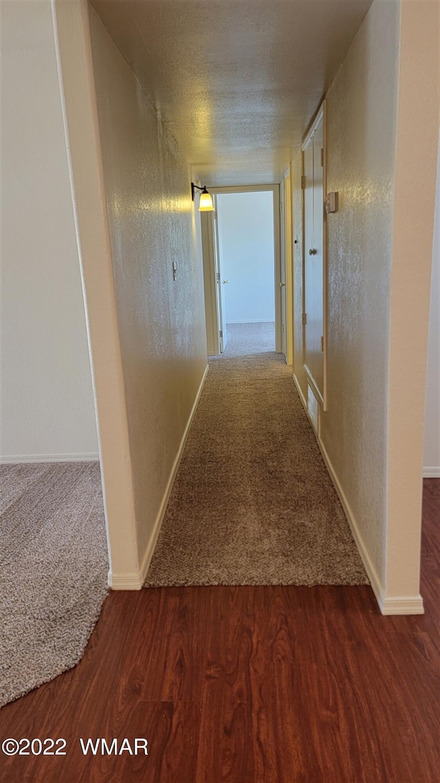 hall featuring visible vents, baseboards, a textured wall, wood finished floors, and a textured ceiling